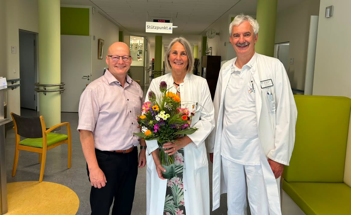 Dr. Röder mit einem Blumenstrauß zwischen Dr. Wellmann (links) und Dr. Menger (rechts)